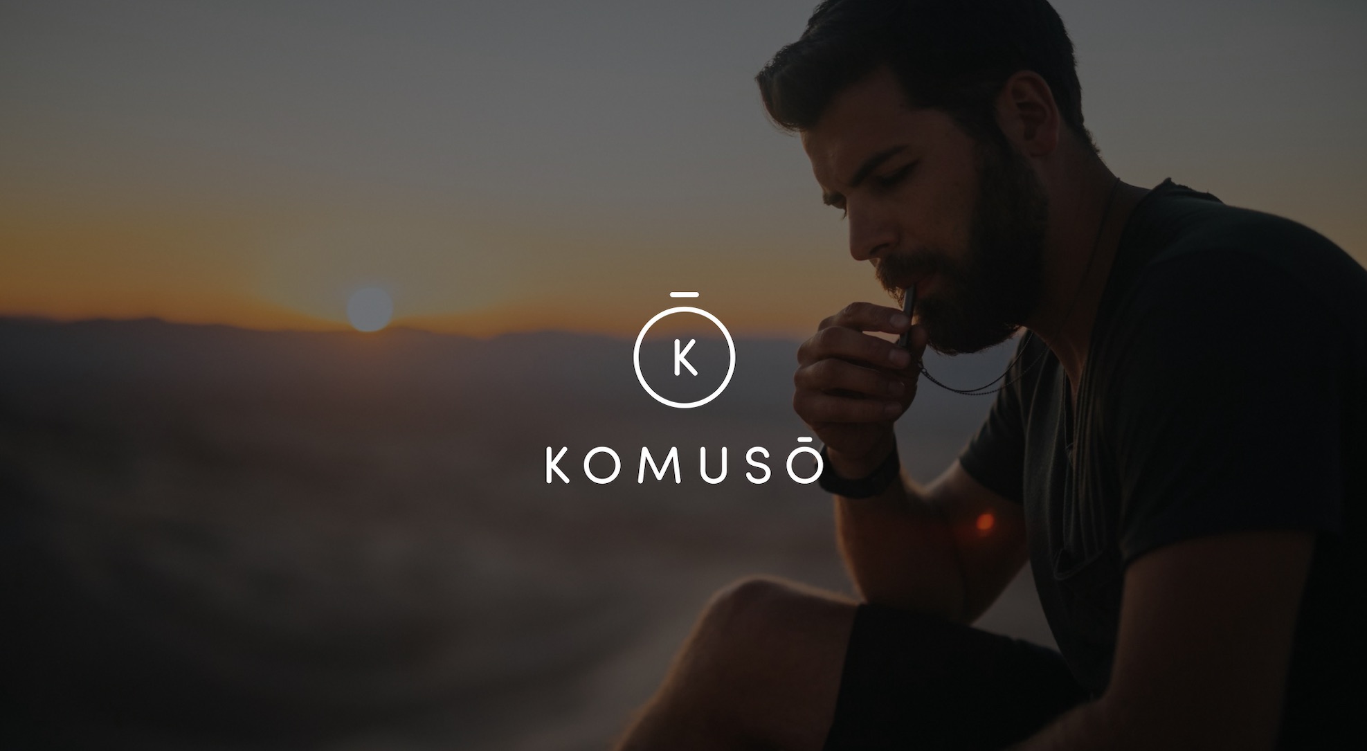 White Komuso logo Photo Services with background of bearded man blowing whistle with sun setting in the distance