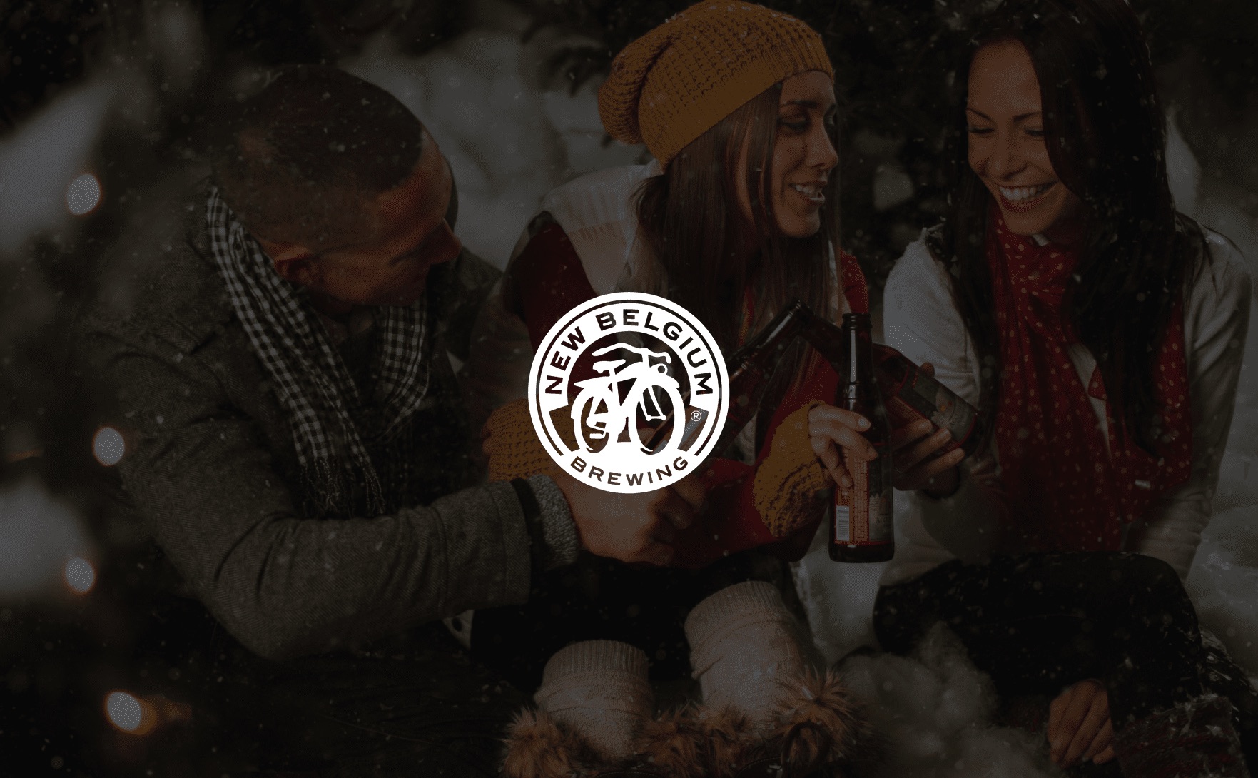 IU C&I Studios Page White New Belgium Brewing logo with man and two women toasting beer bottles in a winter scene in the background