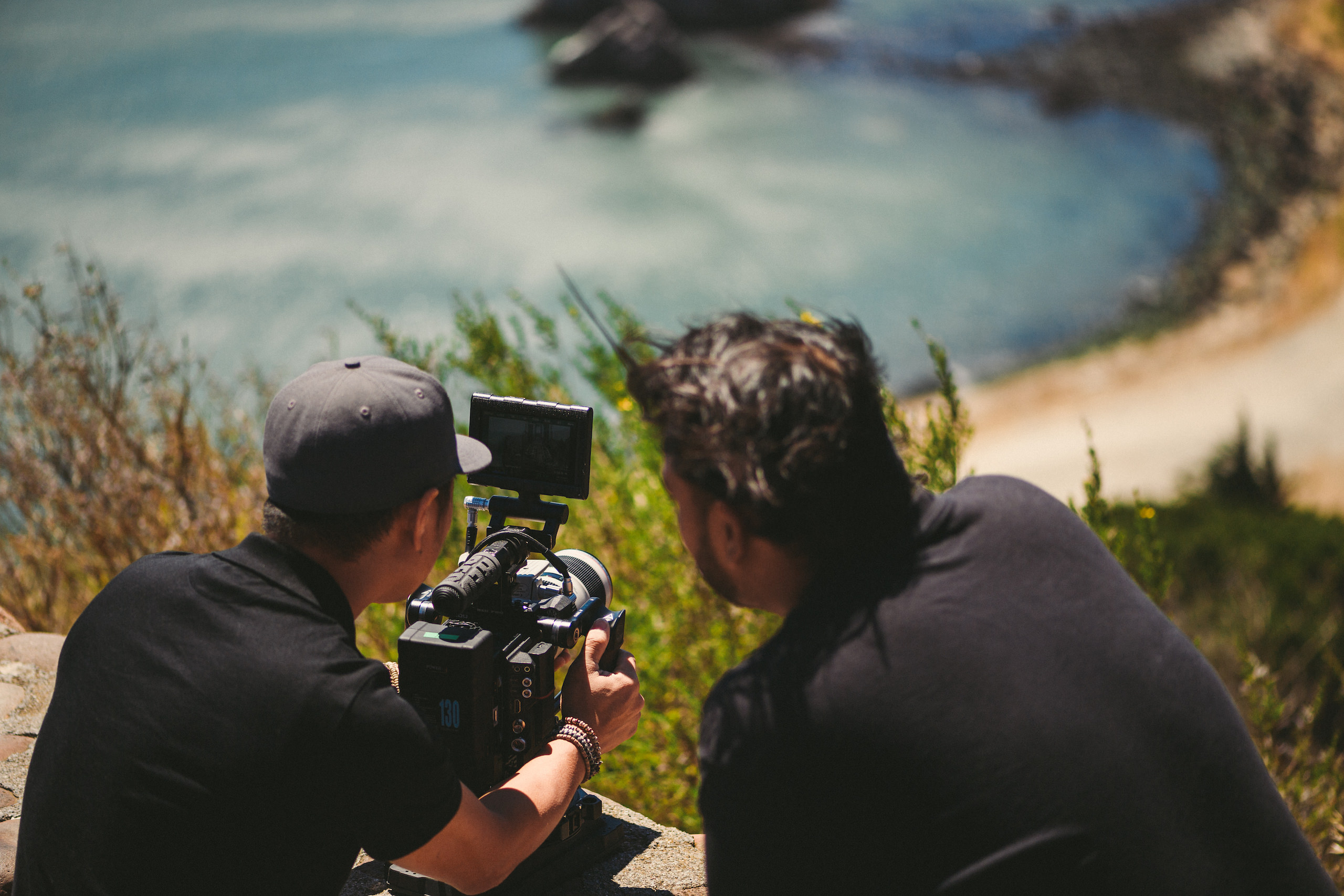 View from behind of two videographers working with a video camera by a lake