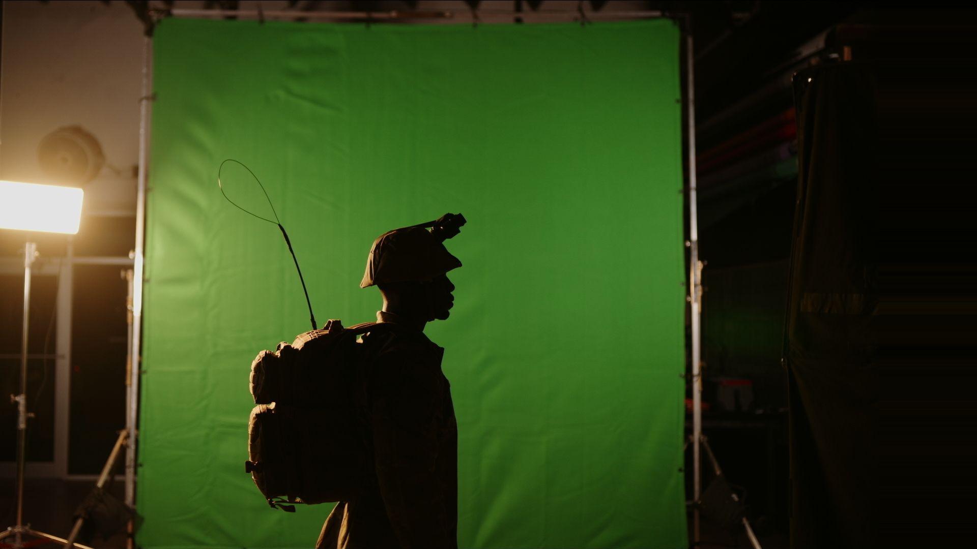 The versatility of a green screen in film production and where to find a professional video company that has one Side profile silhouette of a solder wearing gear in front of a green backdrop in a studio