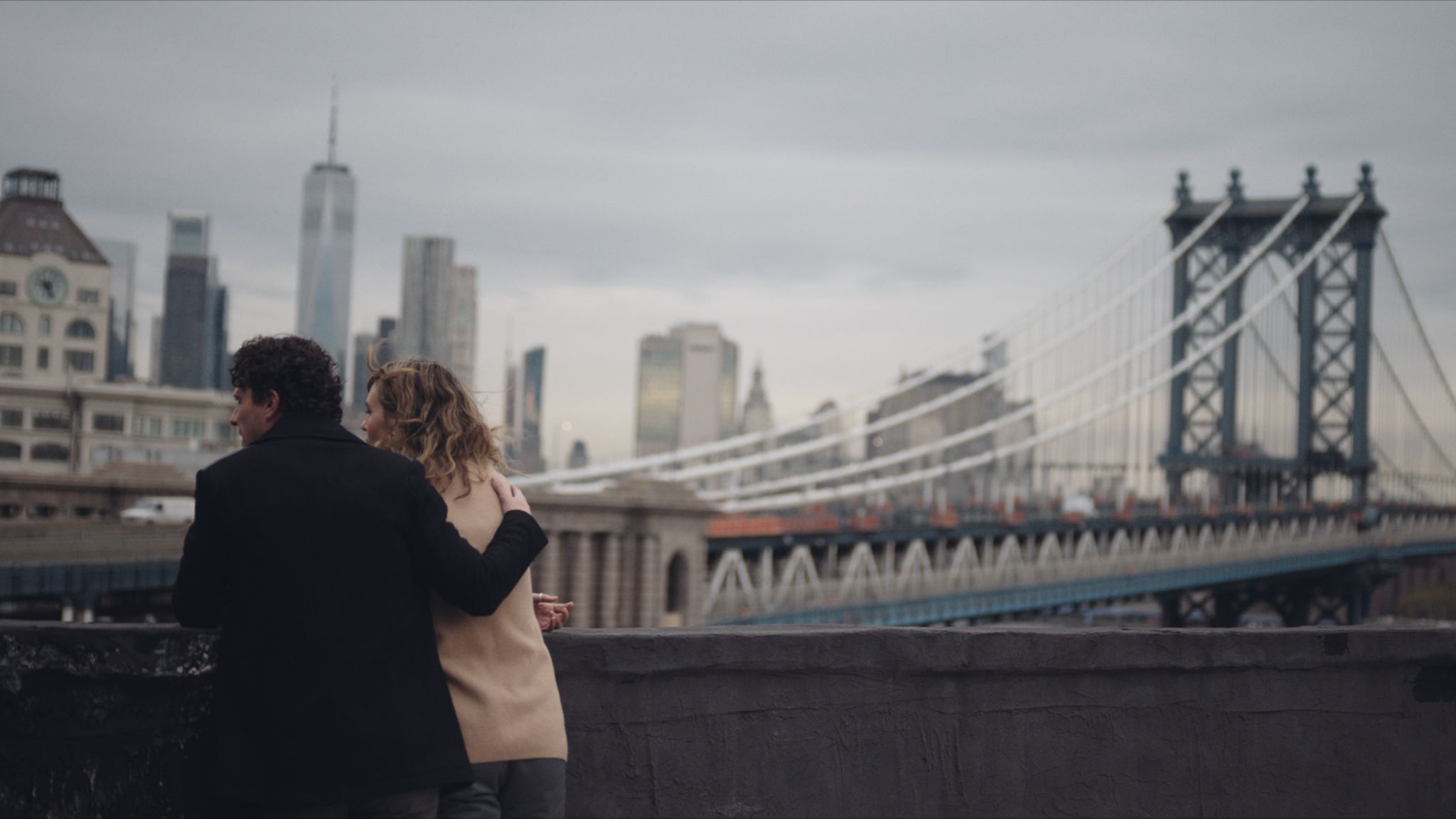 The Rise of the Docuseries Are We in a Documentary Production Golden Age View from behind of man and woman on a bridge with the man's arms around the woman's shoulder looking out at another bridge in New York City