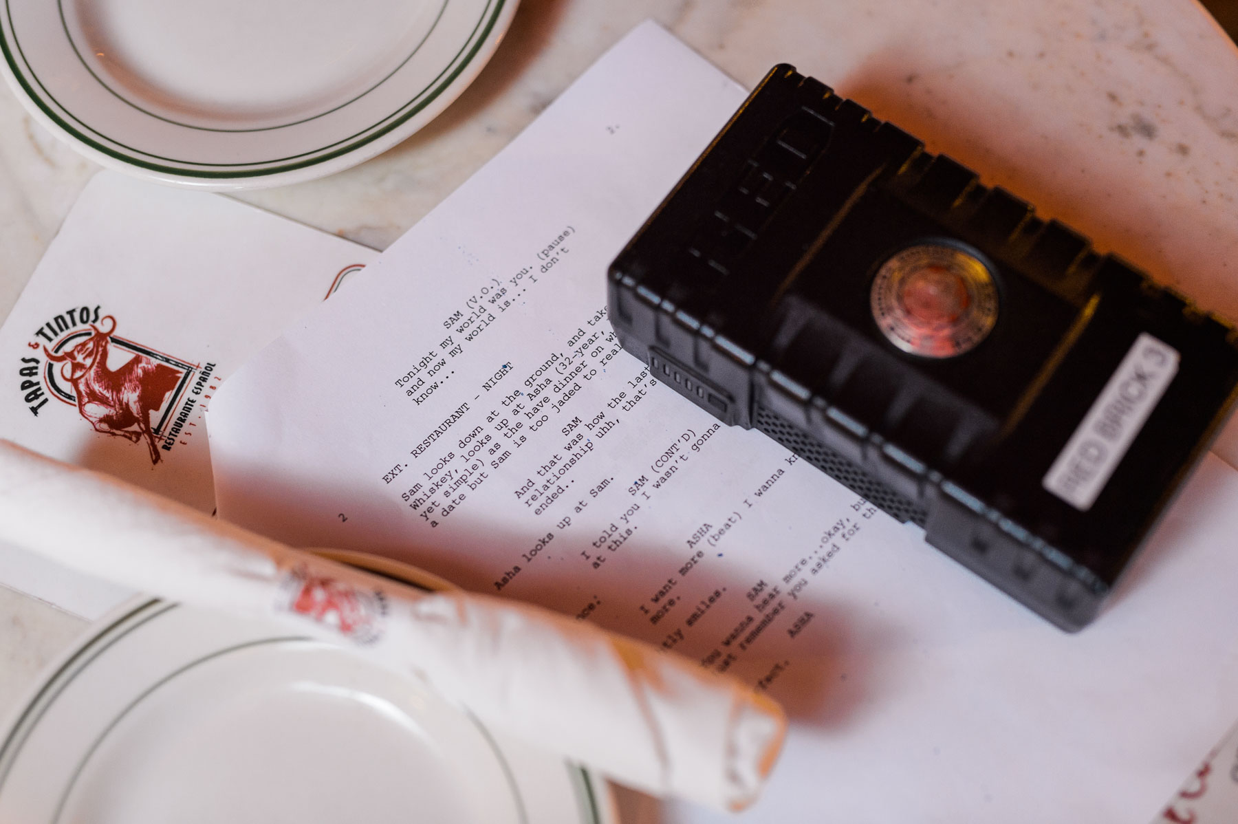 Tips from Film Professionals on Pre Producing a Documentary Closeup of Red Brick on script by a white plate and silverware wrapped in a napkin