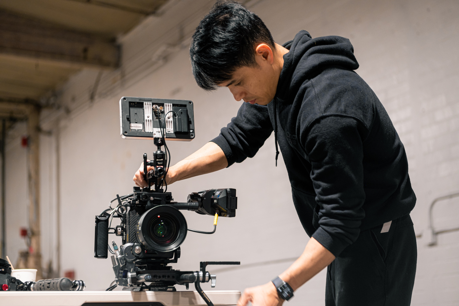 Longform Content Side profile of a male crew member wearing a black sweater and sweatpants setting up a video camera