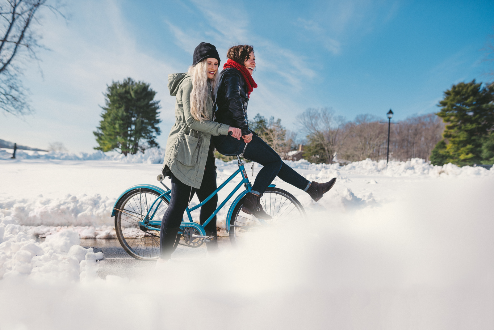 Video Marketing ideas for Winter Holidays Side profile of two women smiling wearing winter gear on a bicycle with one sitting on the handlebars going through the snow