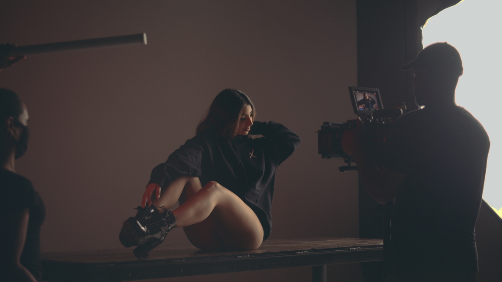 View from behind of Joshua filming a woman posing wearing a black cropped sweatshirt