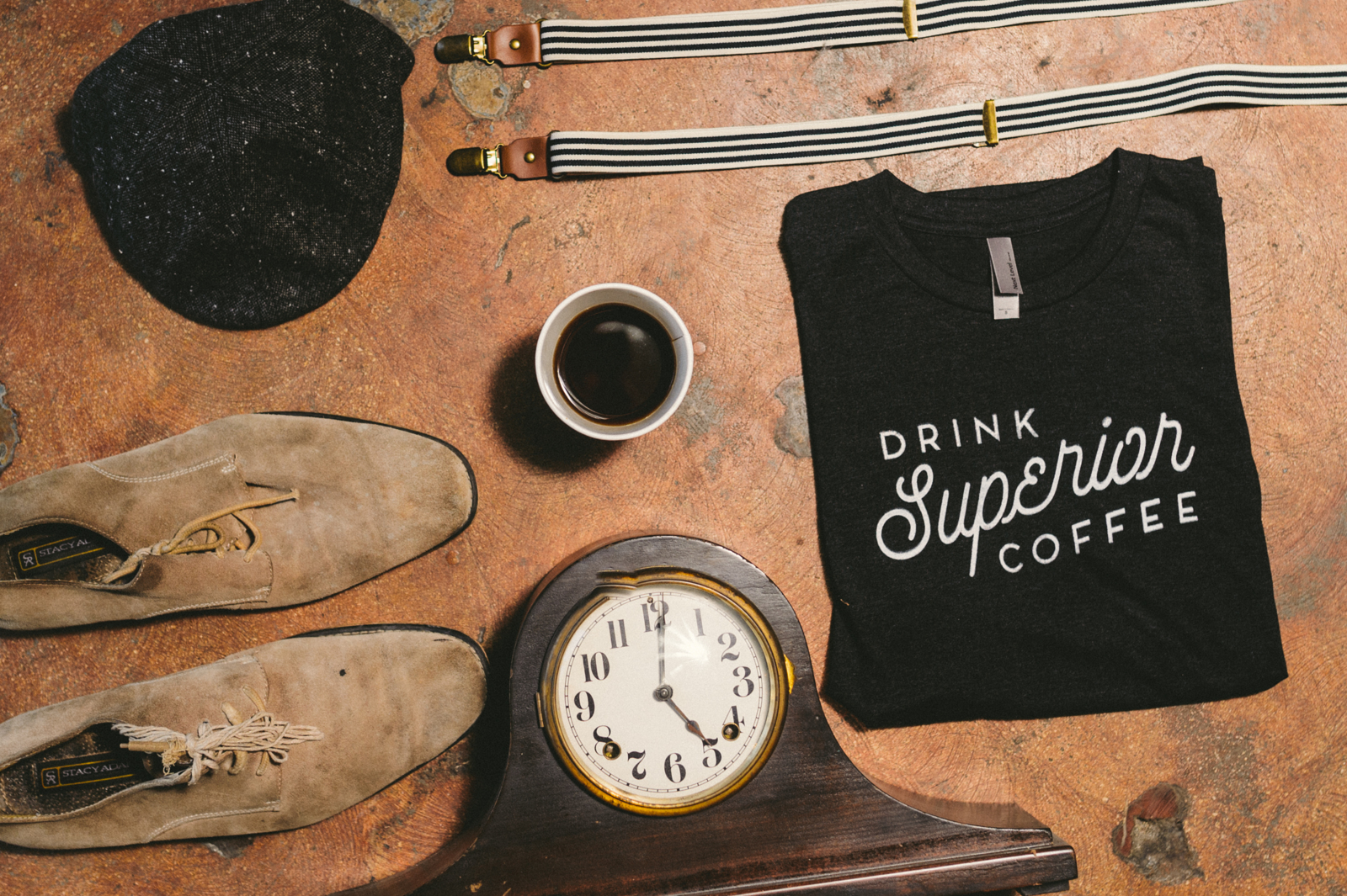 The Benefits of Creating Content en Masse Leather shoes, old mantle clock, black t shirt that says Drink Superior Coffee a coffee cup of coffee, a black cap and striped suspenders on display