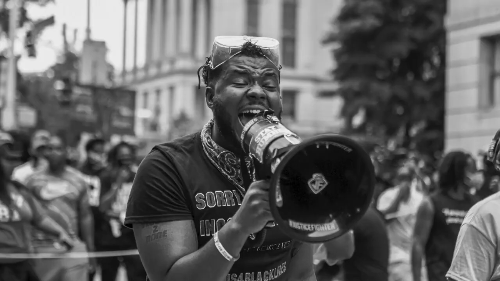 How Video Content can Support your HR team Black and white headshot of an African American man with googles on his head holding a bullhorn talking to the crowd in a city