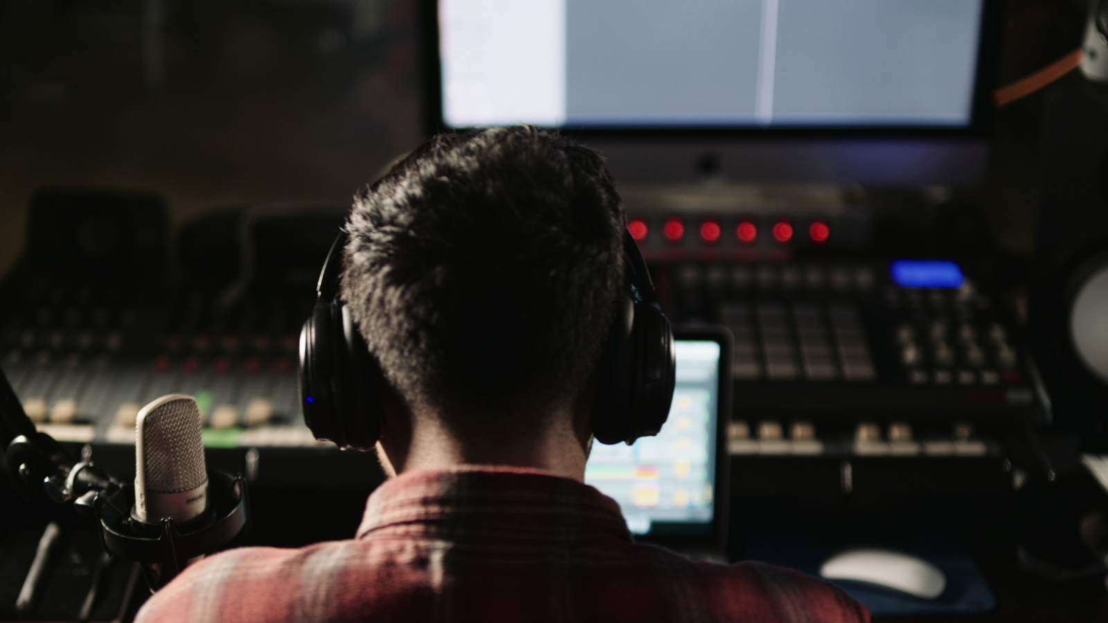 Key Components of Sound Design in Films and TV Shows Foley composer score etc View from behind of man wearing black headphones a red shirt working on a laptop