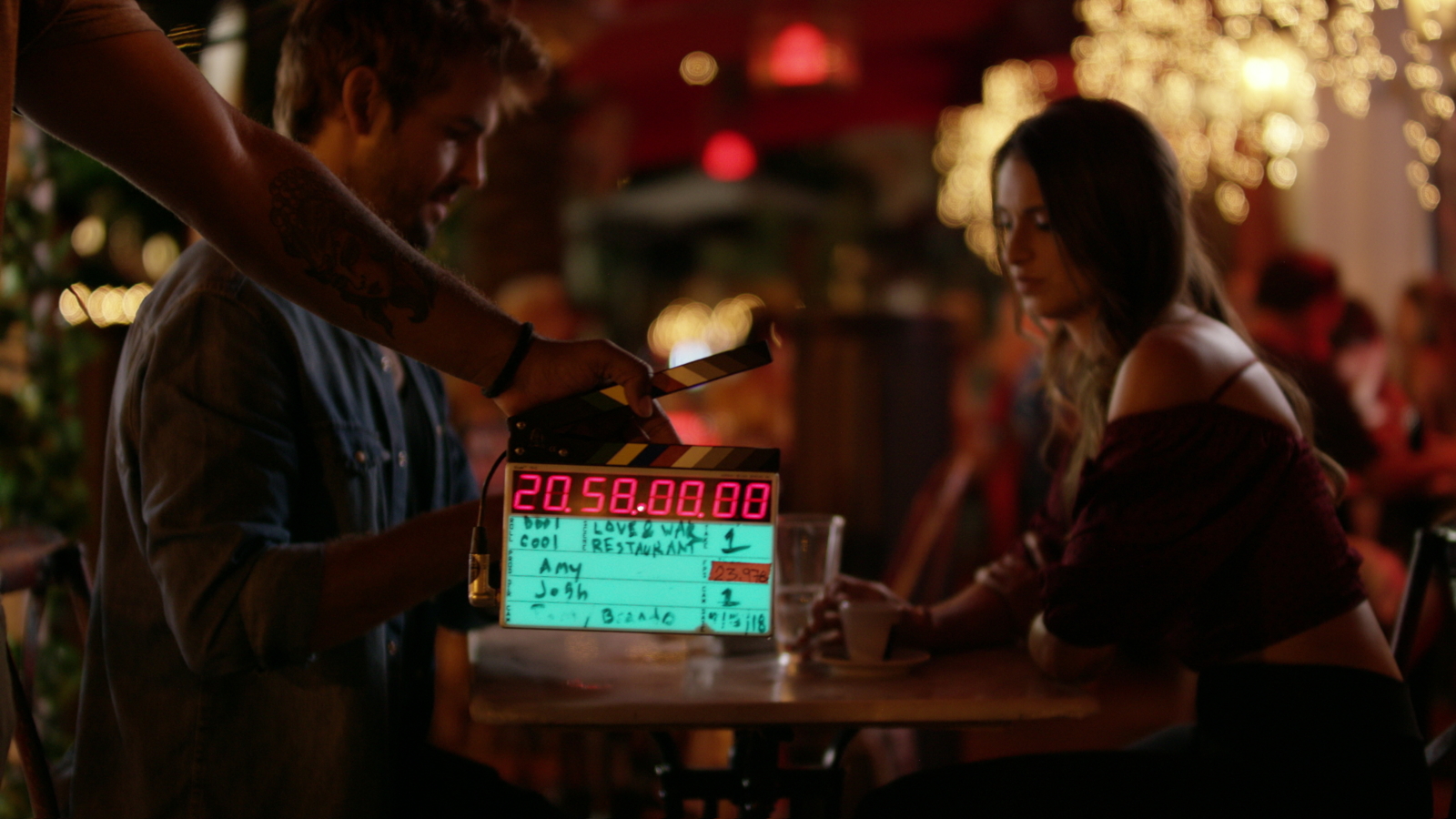 Digital clapboard being used in front of man and woman on a restaurant set