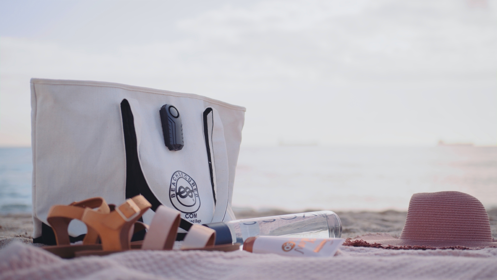 What Your Amazon Ads are Missing Black and white Beachsecured bag in the sand with brown sandals, lotion, water bottle as well as pink hat and beach towel