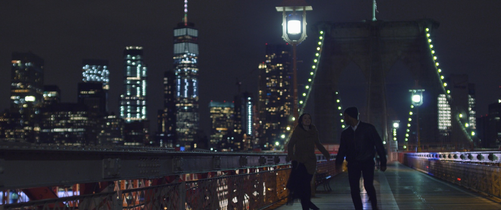 Man and woman walking on a bridge at night by a city