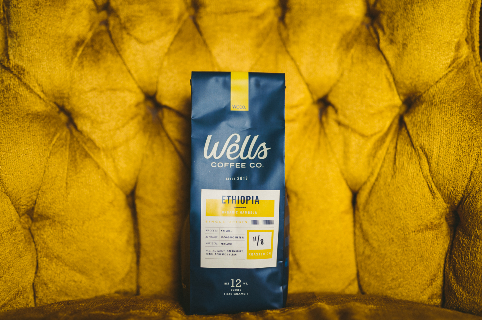 Bag of Ethiopia version of coffee from Wells Coffee Co on display on mustard colored plush chair