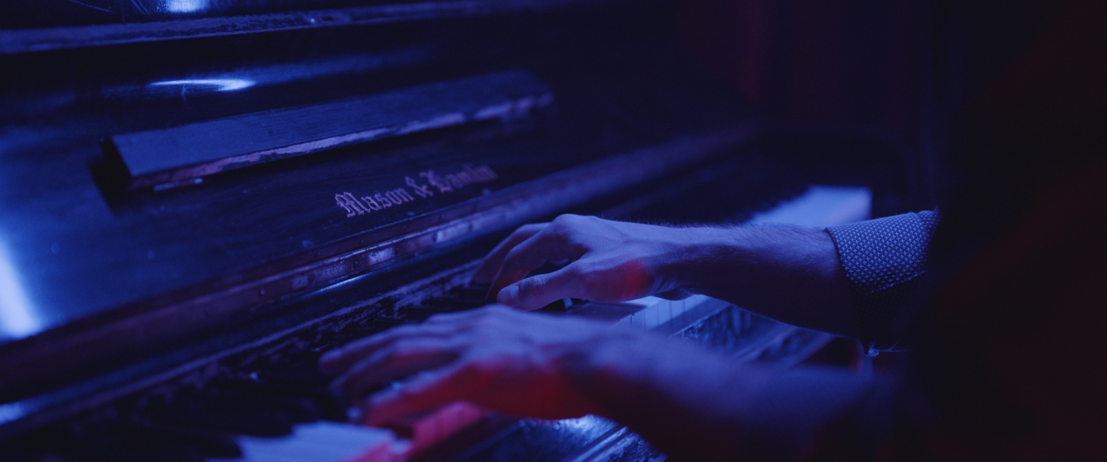 The Role of Music in Film and TV Production Side profile closeup of person playing keyboard in purplish bluish light