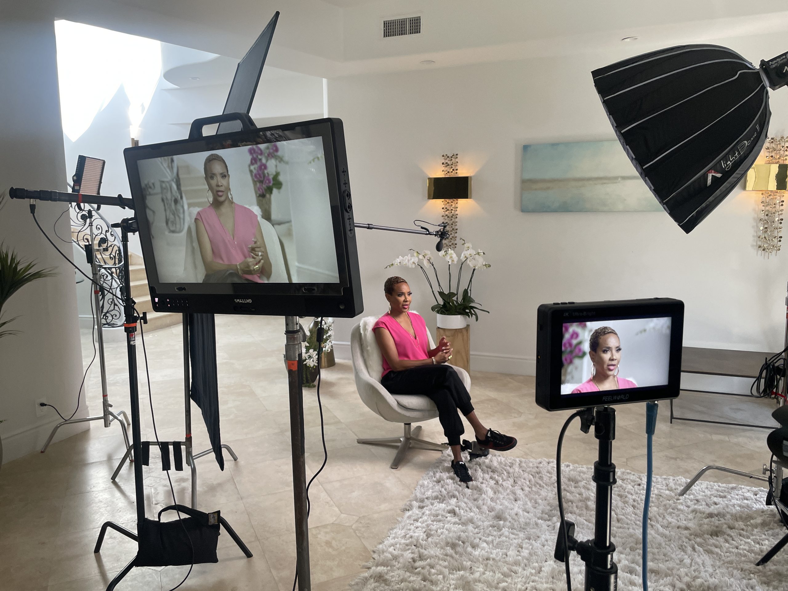 BlackPopBTS MC Lyte by CI Studios Closeup of video displays with her sitting on a white chair wearing a pink dress top along with black pants and shoes