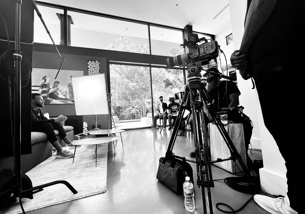 Documentary Film Production BlackPopBTS Steph Curry by CI Studios with black and white of him on set sitting on a couch with tables near him along with crew and equipment