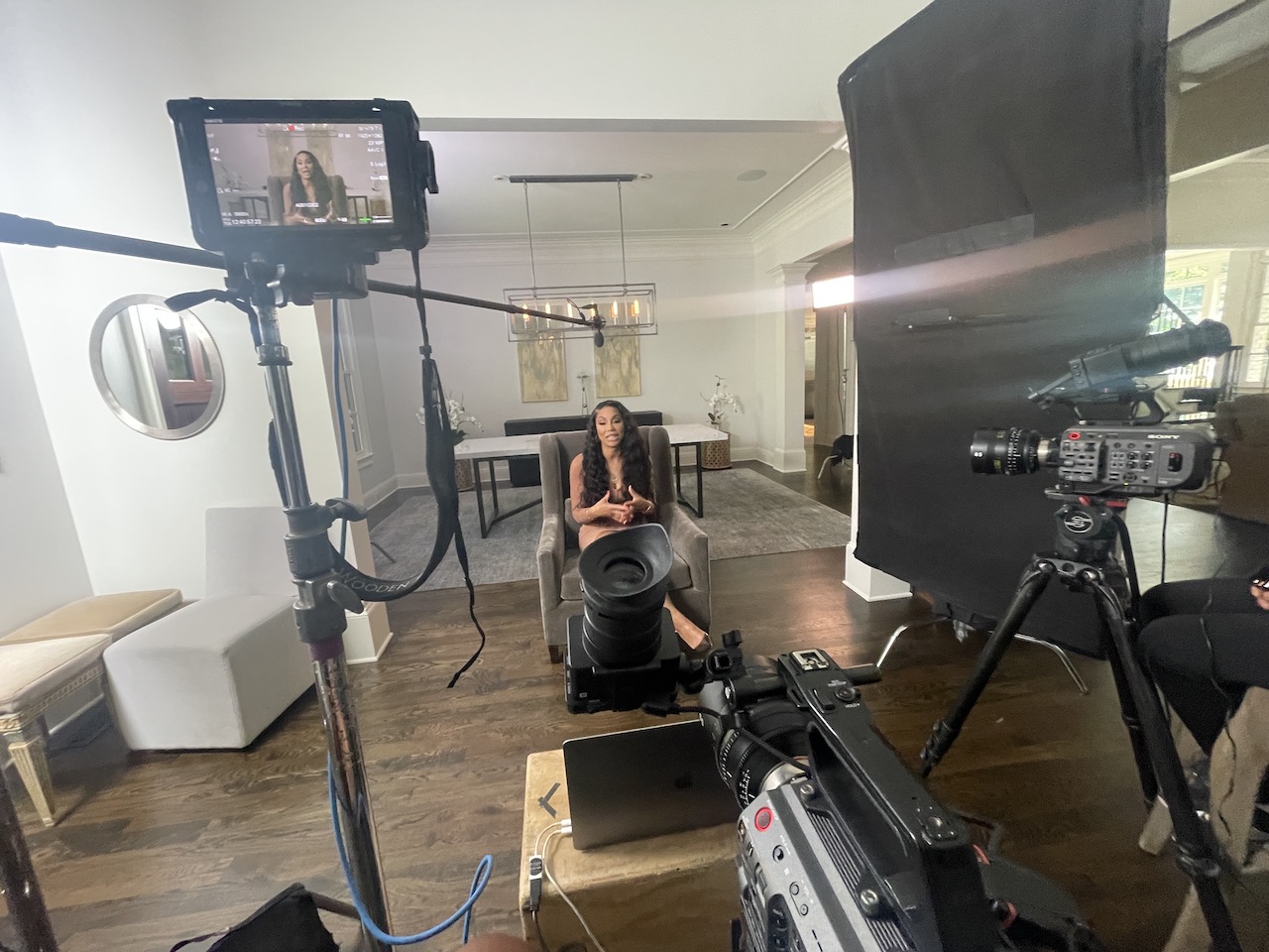 BlackPopBTS Tamar Braxton by CI Studios with her with long brown hair sitting on a gray chair talking with equipment around