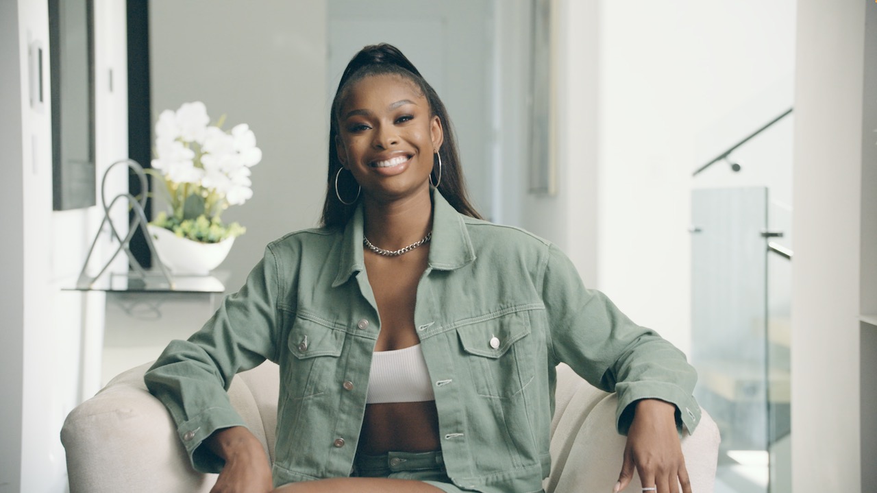 Black Pop Coco Jones headshot of her smiling wearing a light green jean jacket and jean shorts
