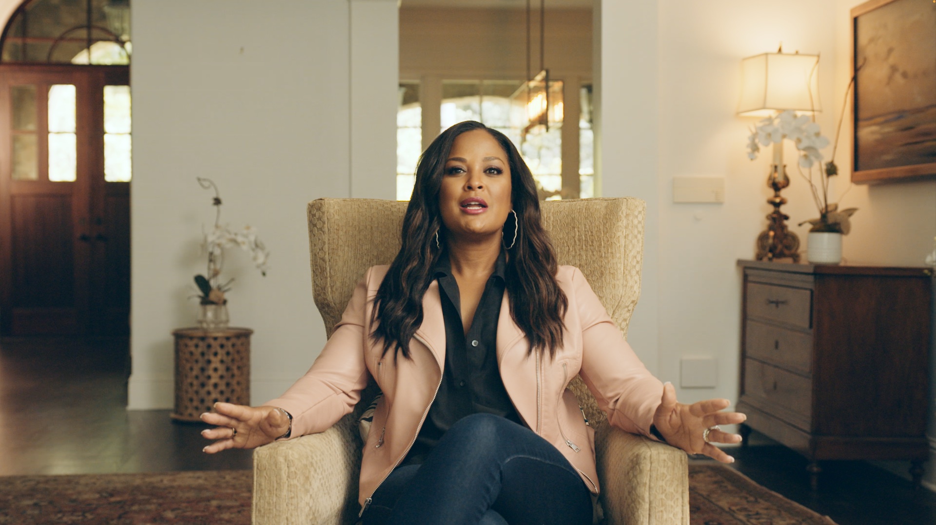 Black Pop Laila Ali headshot with her talking to the camera sitting in a beige chair