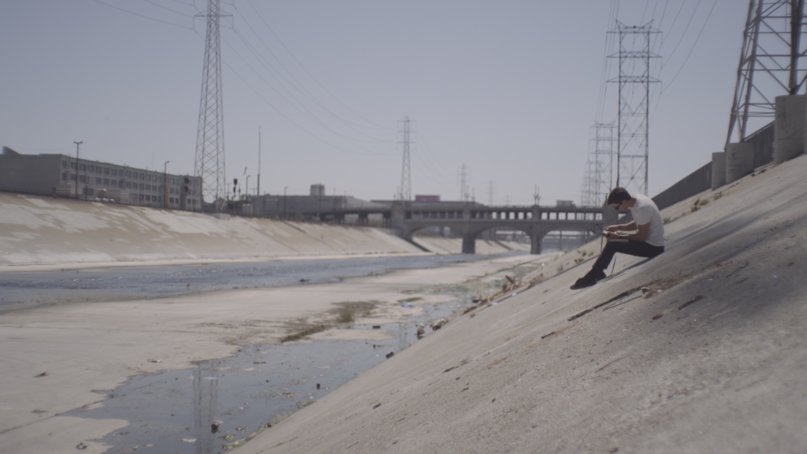 Side profile of man wearing white t shirt and jeans sitting on a bank of a culvert