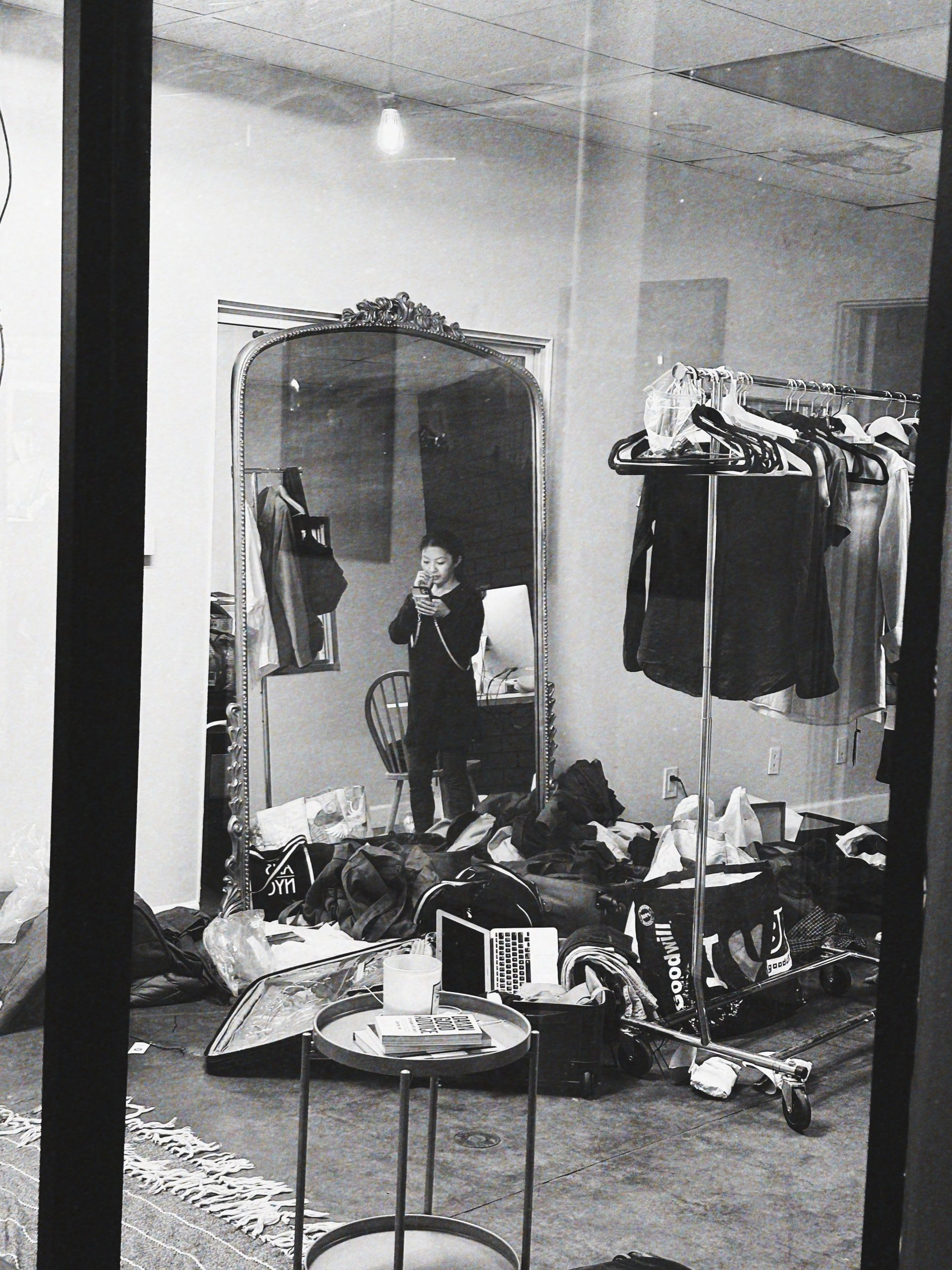 IU Black and white of Asian wardrobe film crew member organizing clothing items in wardrobe room for The American Film