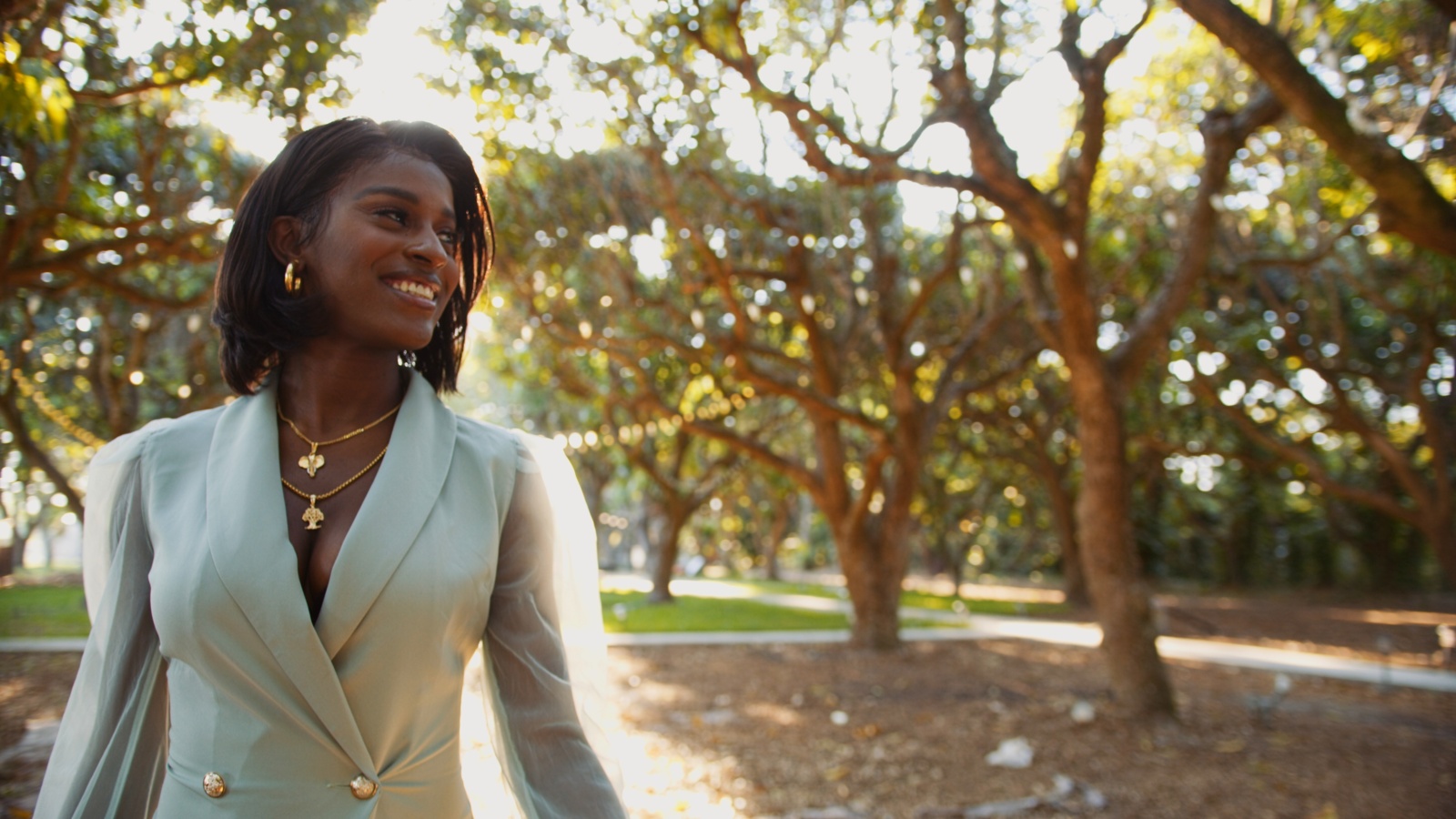 African American woman wearing a white dress coat looking off to the side smiling in a park