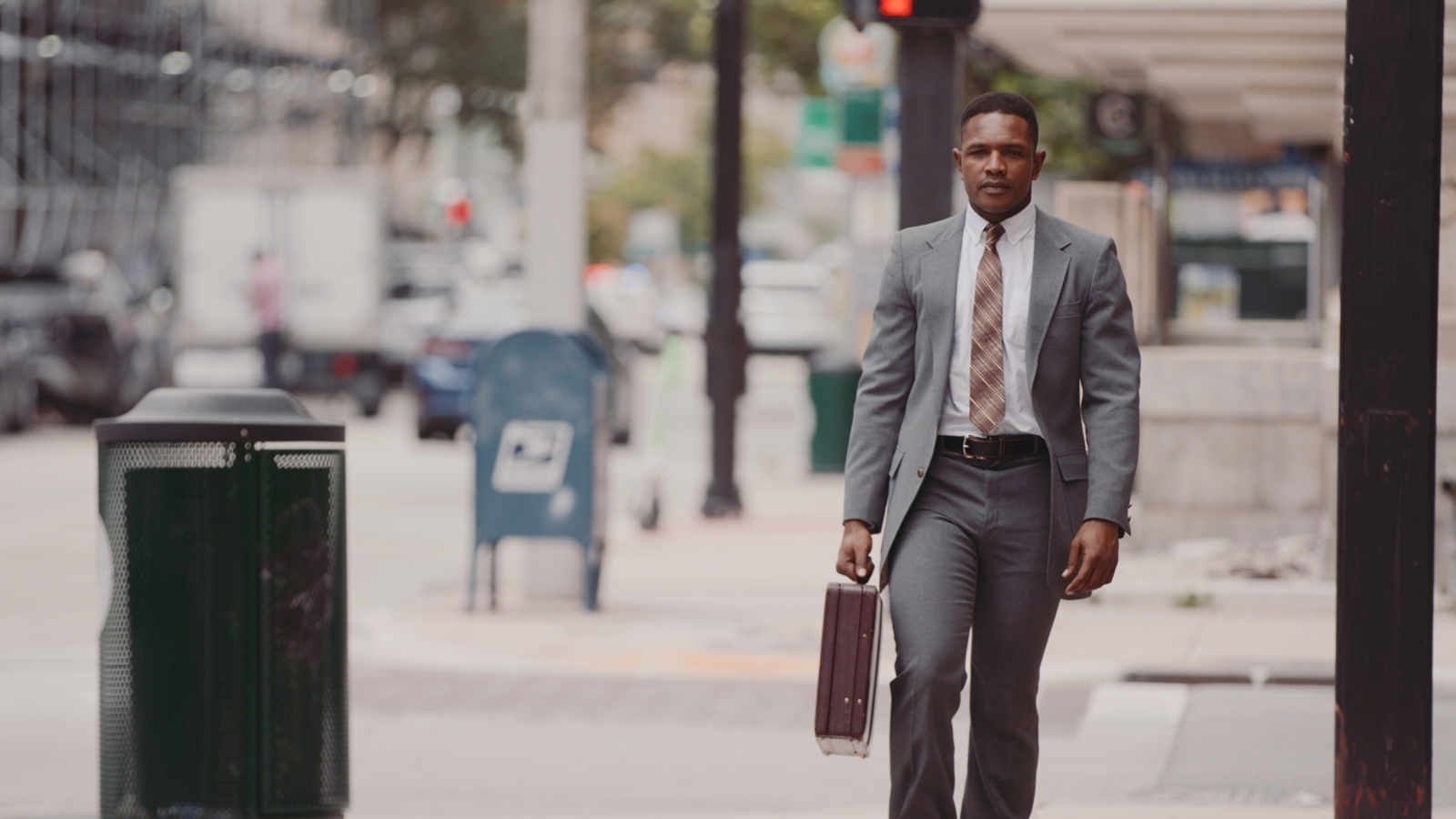 African American man walking down a city street wearing a gray suit carrying a brown briefcase