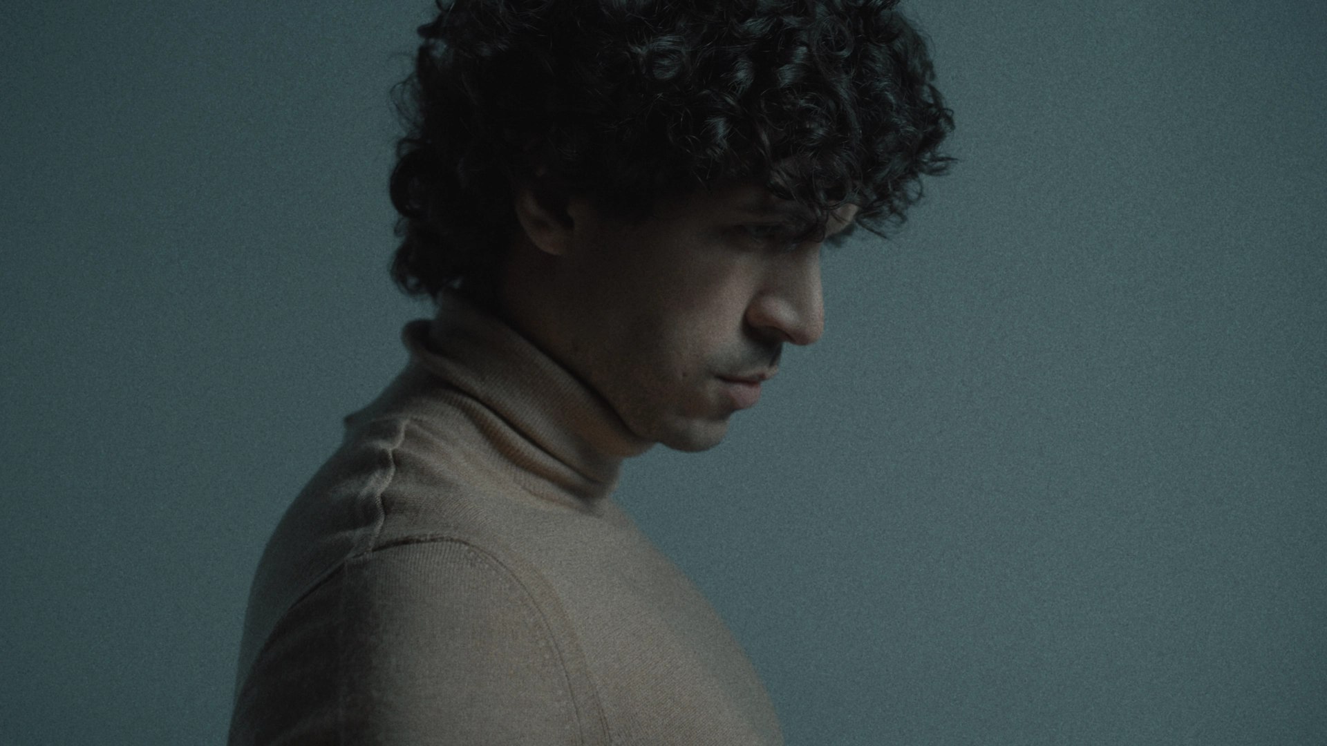 Side profile headshot of man with curly hair looking down