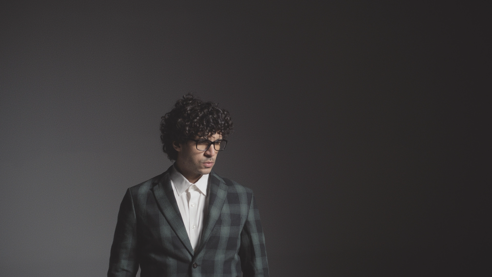Man with curly hair wearing glasses wearing a blue checkered suit