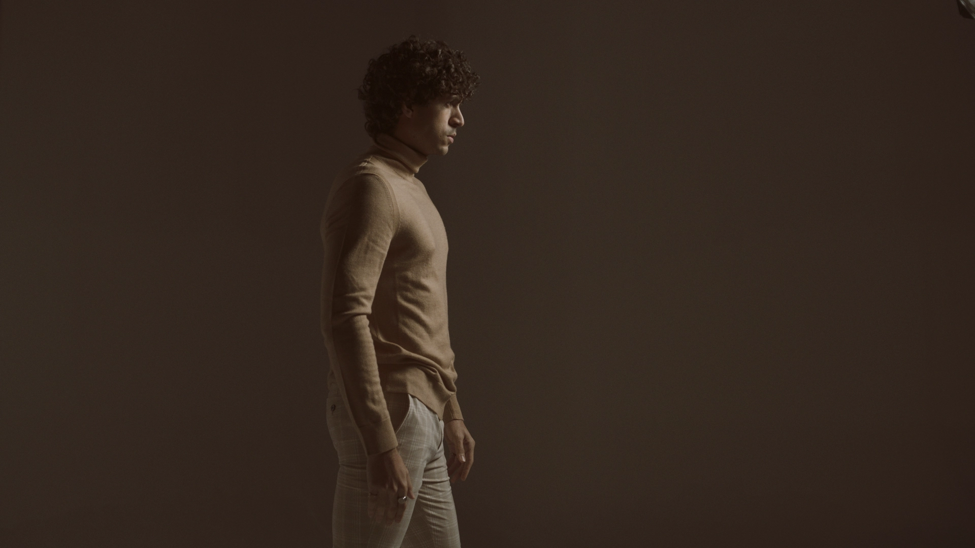 Side profile of man with curly hair wearing beige sweater and patterned pants