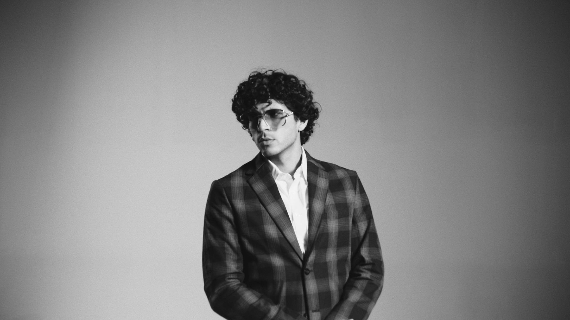 Headshot of man with curly hair wearing glasses posing in a suit