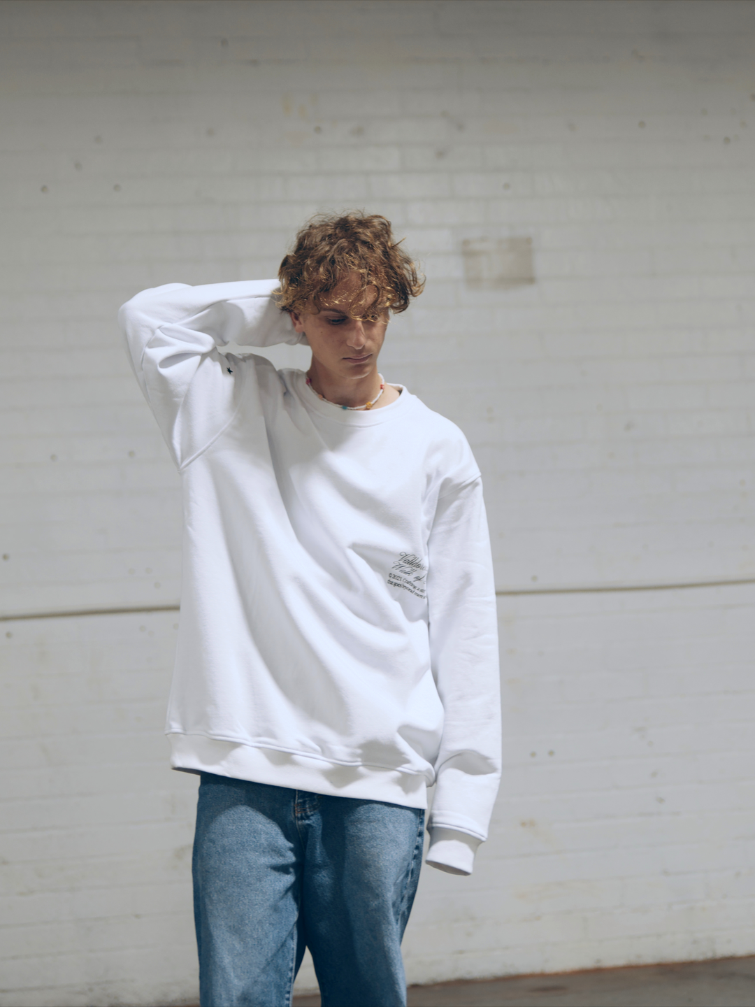 Male apparel model posing outside wearing a white long sleeve sweater.